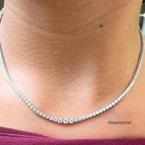May include: A delicate, sparkling necklace featuring a row of round-cut diamonds. The diamonds are set closely together, creating a continuous line of brilliance. The necklace is worn around the neck, resting on the skin. The word "dreamystar" is visible.