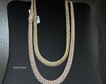 May include: Two gold-colored, diamond-studded cuban link necklaces displayed on a black jewelry stand. One necklace is a lighter gold color, and the other is a rose gold color. The necklaces are clasped at the top.