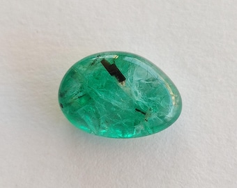 May include: A polished, oval-shaped emerald gemstone. The gem is a vibrant green color with internal inclusions and a high degree of transparency. The stone has a smooth, rounded shape, and is set against a white background.