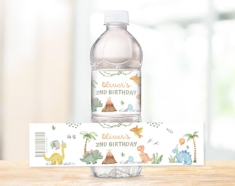 Może przedstawiać: Przezroczysta plastikowa butelka wody z etykietą z akwarelowymi dinozaurami, wulkanami i palmami. Na etykiecie widnieje napis "Oliver's 2nd Birthday" złotymi literami. Butelka stoi na drewnianej powierzchni.