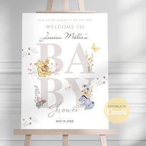 Peut inclure: Panneau de bienvenue pour une baby shower sur un chevalet. Le panneau présente le texte "Bienvenue à la baby shower de Jessica Miller" avec des personnages de Winnie l'ourson et des accents floraux. La date "18 mai 20XX" est également affichée.