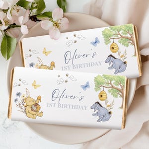 May include: Two chocolate bars with gold edges, featuring illustrations of Winnie the Pooh characters, butterflies, and bees. The text "Oliver's 1st Birthday" is displayed in elegant script. The bars are presented on a white plate.