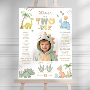 May include: A personalized birthday poster on an easel. The poster features a photo of a toddler in a dinosaur costume, with text that reads "Oliver is a Two-Rex." It includes favorite foods, toys, songs, and nicknames. The poster is decorated with dinosaur illustrations.