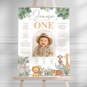 Può includere: Un cartello di compleanno con una foto centrale di un bambino con cappello da safari, circondato da dettagli testuali tra cui nome, età, cibi, giocattoli e canzoni preferite. Il design include illustrazioni ad acquerello di zebra, rinoceronte, leone, scimmia, giraffa, elefante e tigre, con testo che indica 20 pounds, 6 teeth e 25 inches.