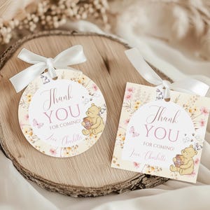 Puede incluir: Dos etiquetas de regalo con el tema de Winnie the Pooh. Una es redonda, la otra cuadrada. Ambas tienen un diseño floral, el texto "Thank You For Coming!" y una pequeña ilustración de Winnie the Pooh con un tarro de miel. Cada etiqueta tiene una cinta blanca.