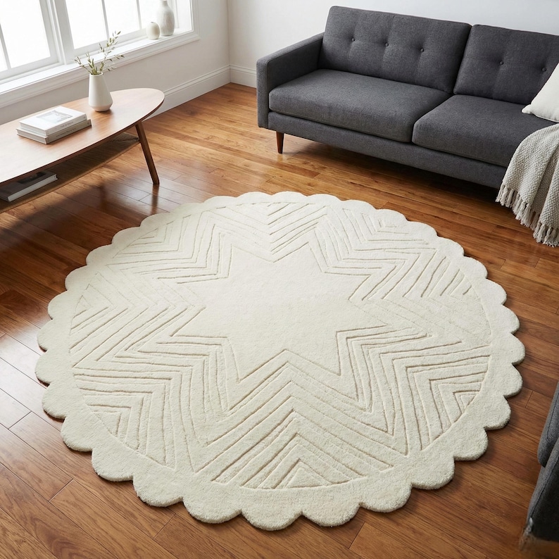 May include: Cream-colored, round rug with a scalloped edge and a large star design in the center. The star pattern is created with linear, geometric shapes. The rug is placed on a hardwood floor, and the room has a modern aesthetic.