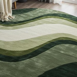May include: A round area rug with a wavy design in shades of green and off-white. The rug has a soft, textured appearance and is placed on a hardwood floor. A cream-colored throw blanket with fringe is draped over a gray sofa.