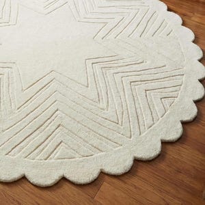 May include: Cream-colored, round rug with a star design. The rug features a scalloped edge and a textured surface. The star pattern is created with linear indentations, adding depth and visual interest to the floor covering.