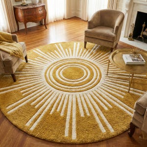 May include: A round, mustard yellow rug with a sunburst design. The rug features a central circle with concentric rings, surrounded by radiating white lines. The rug is a decorative element for a living room.
