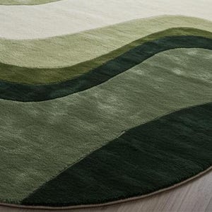 May include: A round rug with a wave pattern in shades of green, from light to dark. The rug has a soft, textured appearance and is placed on a light-colored wooden floor. The design creates a sense of depth and movement.