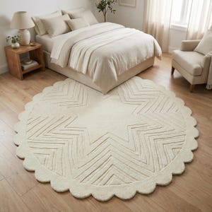 May include: Cream-colored, round rug with a scalloped edge and a large star design in the center. The star pattern is made of zig-zag lines. The rug is placed on a hardwood floor in a bedroom setting.