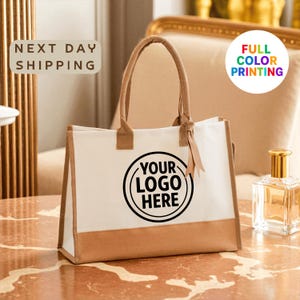 A white tote bag with a black logo printed on it, placed on a marble surface.