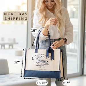 A smiling woman holding a large tote bag with a cruise ship design, standing in front of a window.