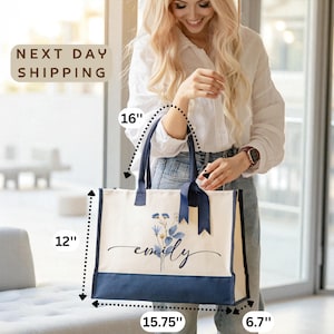 A smiling woman holding a large tote bag with a floral design, standing in front of a window.