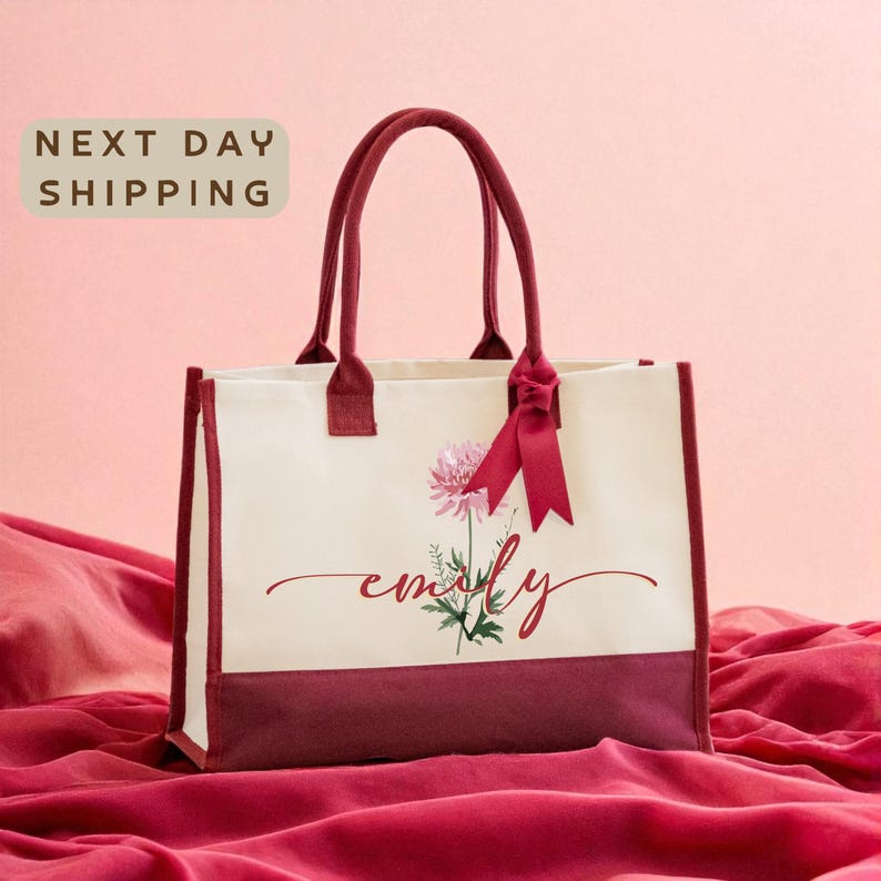 A white tote bag with a red ribbon and a pink flower design, sitting on a red fabric background with the text "Next day shipping" displayed above it.