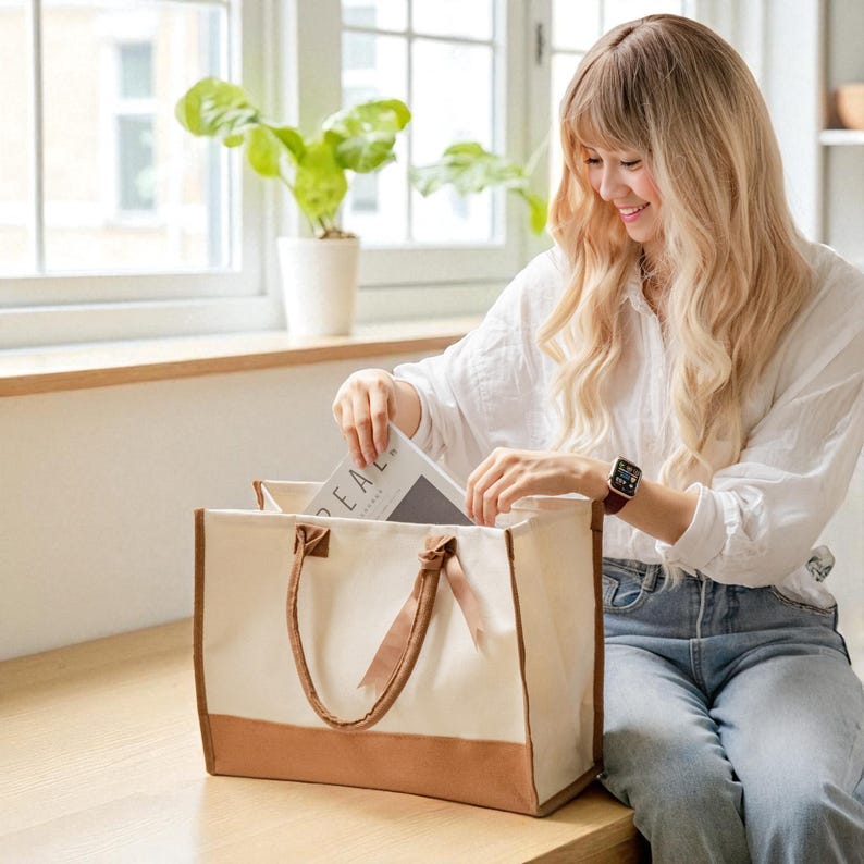 A woman with long blonde hair is sitting on a wooden bench, opening a large tote bag and pulling out a book.