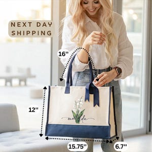 A smiling woman holding a large tote bag with a floral design, standing in a room with a window.
