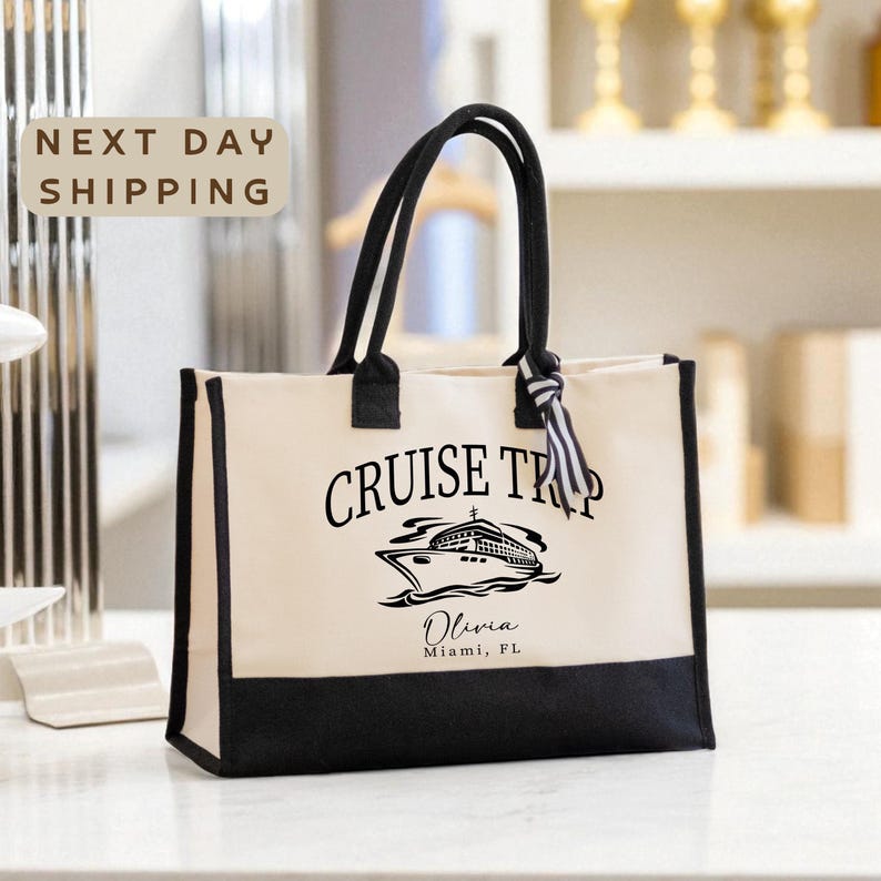 A beige tote bag with the text "CRUISE TRIP" printed on it, along with a graphic of a cruise ship. The bag is placed on a white surface, and there is a sign that says "NEXT DAY SHIPPING" in the background.