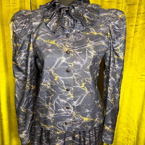May include: A vintage two-piece outfit featuring a dark gray blouse and skirt with a marbled pattern in yellow and white. The blouse has long sleeves, a ruffled collar, and button-down front. The skirt is knee-length.