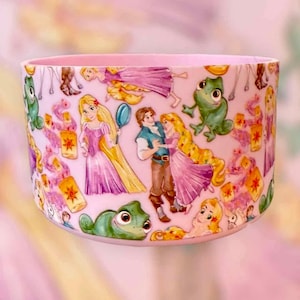 May include: A pink, cylindrical container featuring a repeating pattern of cartoon characters, lanterns, and other elements. The design includes a princess in a pink dress, a man in a blue vest, and a green chameleon. The container has a smooth, glossy finish.
