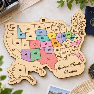 May include: A wooden map of the United States featuring laser-cut state borders and abbreviations. Specific states are filled with light blue, yellow, green, pink, and purple colors. The text Anderson Family Vacation is engraved on the lower right.