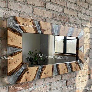 May include: Rectangular wooden mirror with a clear resin and wood grain frame. The mirror is mounted on a brick wall. The text "Bhavya Crafts Co" is printed on the frame.