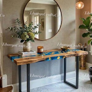 Può includere: Una consolle in legno con intarsi in resina blu e dettagli dorati. Il tavolo ha gambe in metallo nero ed è decorato con un vaso di fiori, libri e una candela. Uno specchio rotondo è appeso alla parete dietro il tavolo. Il testo "Bhavya Crafts Co" è visibile.