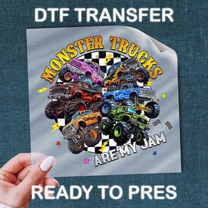 A hand holding a piece of paper with a colorful graphic of monster trucks and the text "MONSTER TRUCKS ARE MY JAM" printed on it.