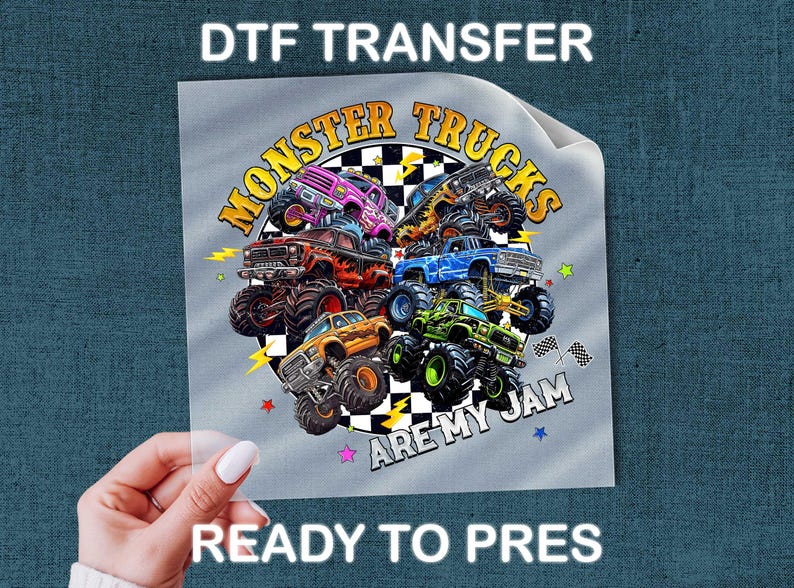A hand holding a piece of paper with a colorful graphic of monster trucks and the text "MONSTER TRUCKS ARE MY JAM" printed on it.