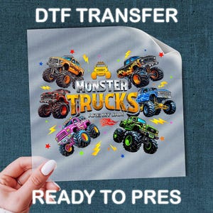 A person's hand holding a piece of paper with a colorful graphic of monster trucks printed on it.