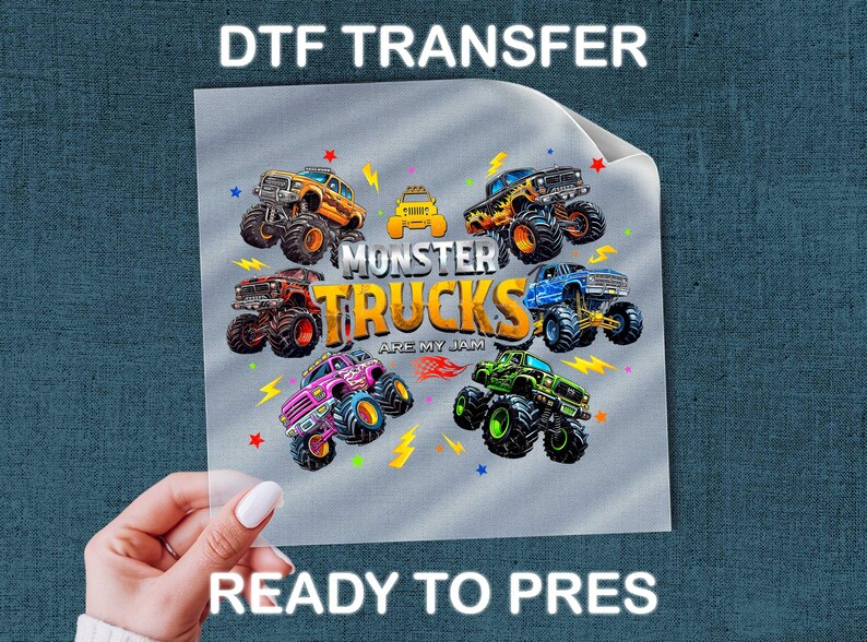 A person's hand holding a piece of paper with a colorful graphic of monster trucks printed on it.