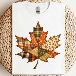 A white t-shirt with a colorful patchwork design of a leaf, resembling a maple leaf, on it.