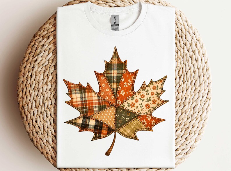 A white t-shirt with a colorful patchwork design of a leaf, resembling a maple leaf, on it.