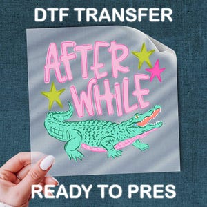 May include: A DTF transfer with the text "AFTER WHILE" in pink, with yellow and pink star accents, and a green alligator illustration. The words "READY TO PRESS" are also visible.