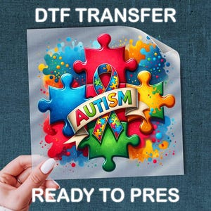 May include: A colorful DTF transfer featuring puzzle pieces in red, blue, green, and yellow, with a ribbon that says "AUTISM". The transfer is ready to press, with the text "DTF TRANSFER" and "READY TO PRESS" in white.
