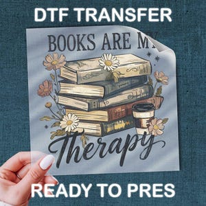 May include: DTF transfer featuring a stack of books with floral accents and a coffee cup. The text "BOOKS ARE MY Therapy" is displayed in a script font. The words "READY TO PRESS" are also visible.