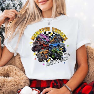 A woman wearing a white t-shirt with a graphic of monster trucks and the text "MonSTER TRUCKS ARE MY JAM" is sitting in front of a Christmas tree.