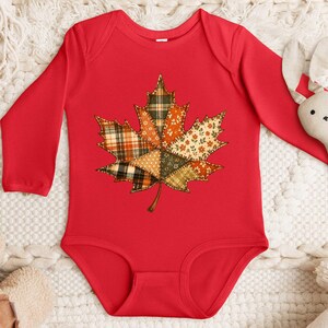 A red onesie with a leaf design, a stuffed rabbit, and a pair of beige slippers are arranged on a white surface.
