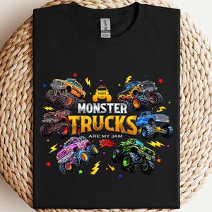 A black t-shirt with a colorful graphic design featuring various monster trucks and the text "MONSTER TRUCKS ARE MY JAM" printed on it.