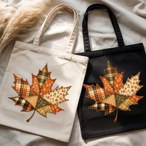 two tote bags with autumn leaf designs, one white and one black, placed on a white cloth.