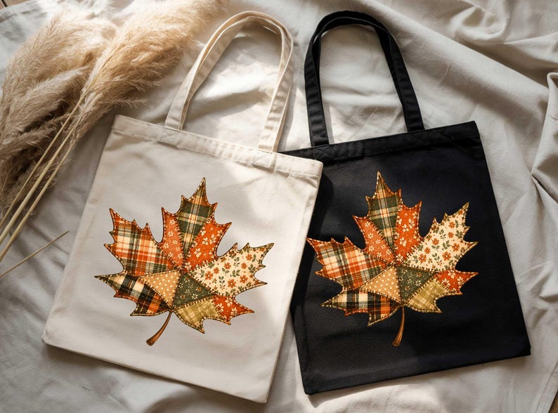 two tote bags with autumn leaf designs, one white and one black, placed on a white cloth.