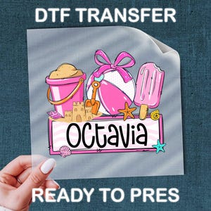 May include: DTF transfer featuring beach-themed graphics. Includes a pink bucket with sand, a beach ball, a sandcastle, a popsicle, and the name "Octavia" in a banner. The words "READY TO PRES" are also visible.