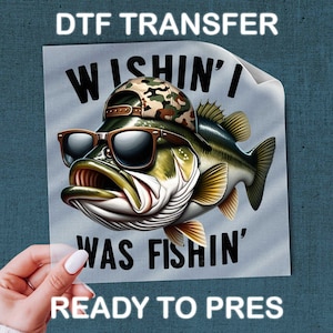 May include: DTF transfer featuring a cartoon bass wearing sunglasses and a camouflage hat. The fish has an open mouth and the text "WISHIN' I WAS FISHIN'" is displayed. The words "READY TO PRES" are also visible.