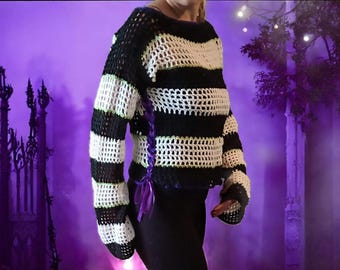 May include: A black and white striped crochet sweater with a loose, open weave. The sweater has long sleeves and is accented with purple ribbon lacing on the side. The overall style is a unique, handmade garment.
