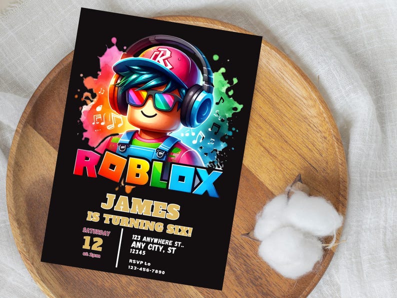 May include: A black invitation card featuring the Roblox logo and a cartoon character wearing headphones and sunglasses. The card reads "JAMES IS TURNING SIX!" with event details. The card is on a wooden plate.