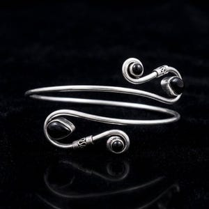 May include: A silver bypass bracelet featuring a spiral design at each end. Each terminal is accented with a smooth, polished black stone, including one teardrop-shaped stone and three round stones set within the metallic silver wire frame.