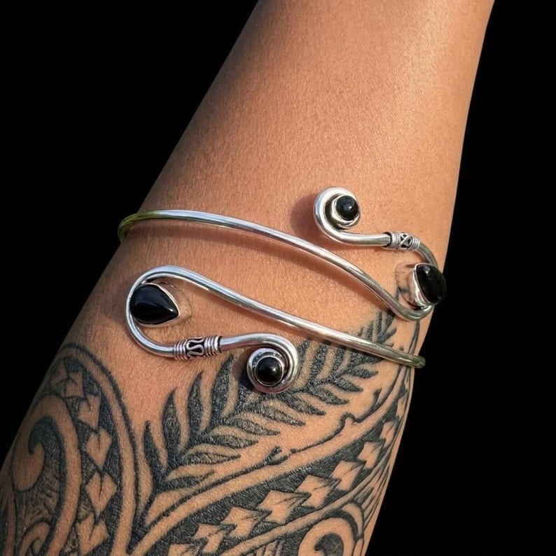 May include: A silver cuff bracelet featuring a bypass design with three black teardrop and round stones. The metal band has decorative wire-wrapped detailing near the ends, which terminate in spiral coils holding the black stones in place.
