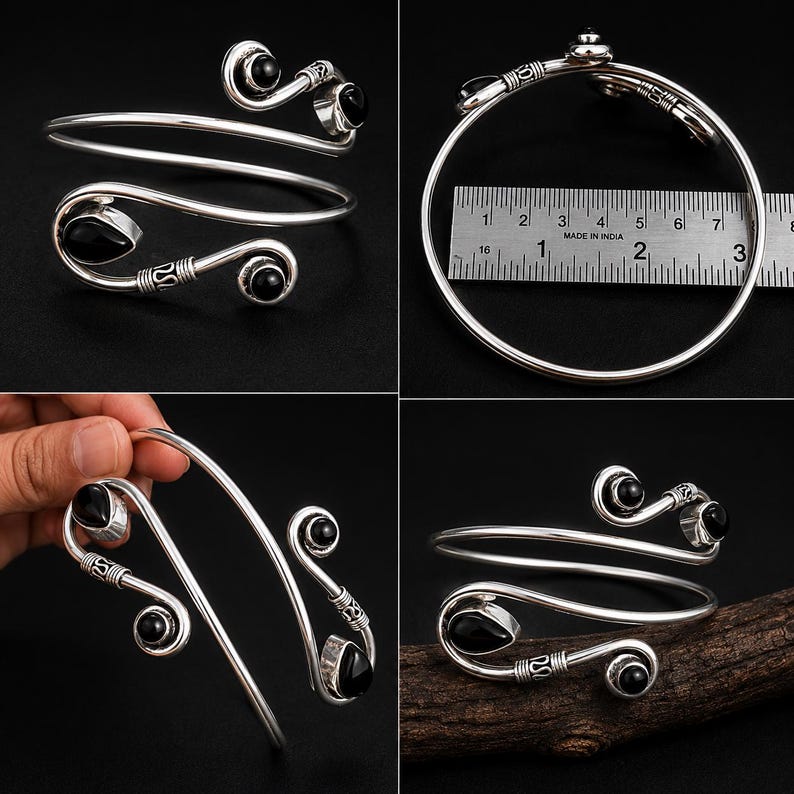 May include: A silver bypass arm cuff bracelet featuring four black teardrop-shaped stones set at the ends of spiraled metal terminals. A metal ruler placed alongside the bracelet indicates a diameter of approximately 3 inches across the band.