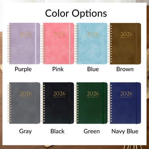 May include: A selection of 2026 planners in various colors, including purple, pink, blue, brown, gray, black, green, and navy blue. Each planner has a gold spiral binding and the year 2026 printed on the cover.
