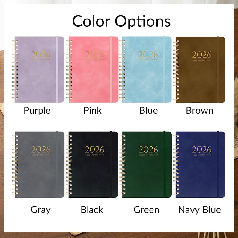 May include: A selection of 2026 planners in various colors, including purple, pink, blue, brown, gray, black, green, and navy blue. Each planner has a gold spiral binding and the year 2026 printed on the cover.